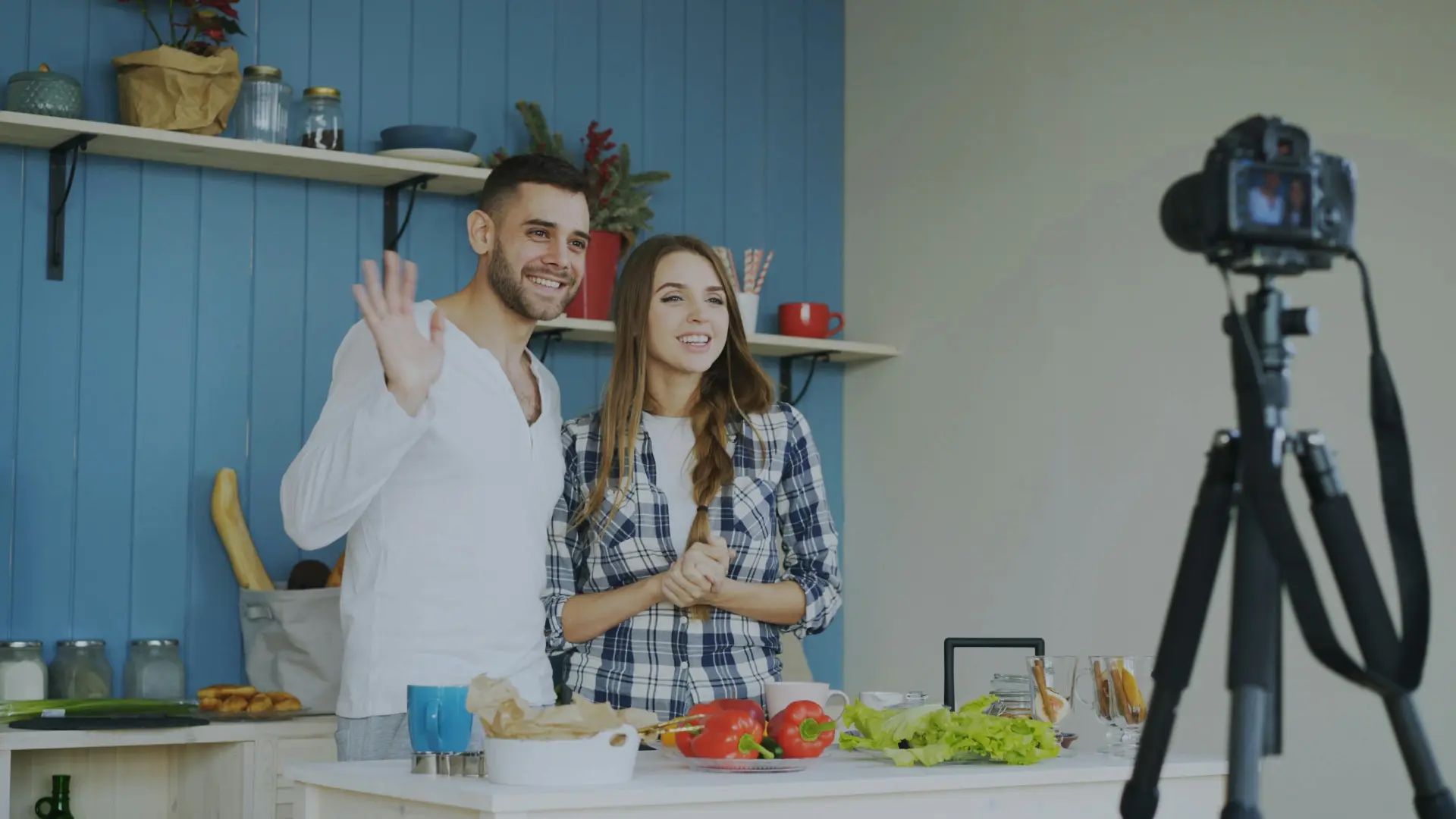 Kobieta i mężczyzna nagrywają film wideo w kuchni na kamerze DSLR na statywie – przykład regularnej produkcji treści wideo